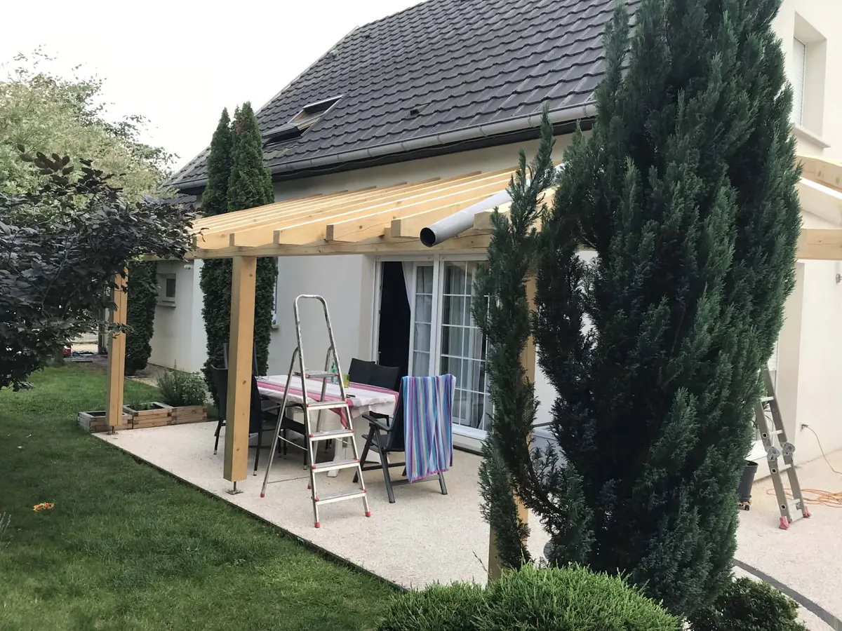 Pergola en bois adossée à une maison, pendant le montage par RAPP Charpente